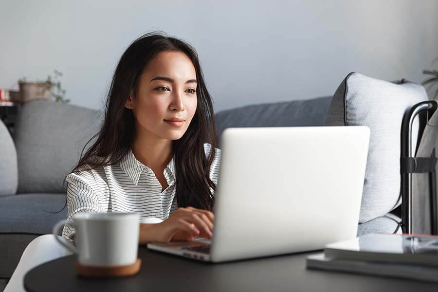 A young woman at her laptop looking at her checking account fees online.